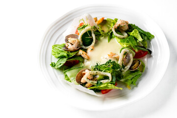 A vibrant, fresh seafood salad featuring shrimp, calamari rings, and clams on a bed of crisp greens and vegetables, served on a white plate.