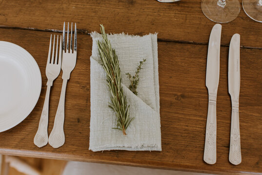 Place setting with napkin and herbs on a rustic wooden table, knife and fork