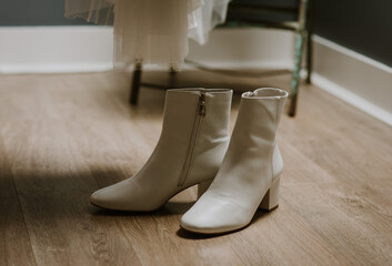 White heeled boots on display on a wooden floor with a wedding dress behind © zoerae28