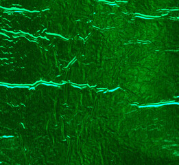 Texture of shiny green foil with numerous wrinkles and folds.