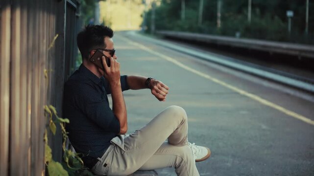 Man Sitting on Railway Platform Waiting for Train and Checking Time 
