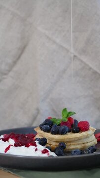 Drizzling Maple Syrup over Crispy Waffles with Fresh Blueberries and Raspberries