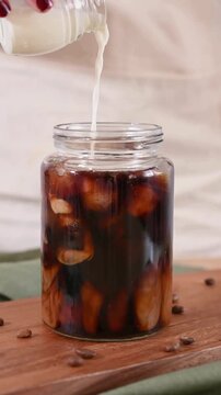 Close Up of Pouring Fresh Milk into Iced Cold Brew Coffee in Glass Jar