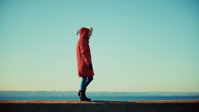 Woman Walking Along Concrete Pier at Sunset. Winter Coastal Promenade