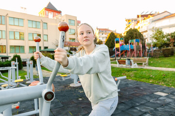 Teenage girl exercising on outdoor fitness equipment in city park, strength training, active lifestyle, healthy habits, urban childhood concept
