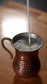 Close-up shot of ayran being poured into a traditional hammered copper cup, creating natural foam. Authentic Turkish yogurt drink served in a classic metal cup. Ideal for Turkish cuisine, beverage, tr