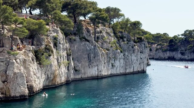 Cassis, France - 14 July 2025: Young people jumping from the cliff into the water at Port Miou calanque in the Calanques National Park, captured from the sea.