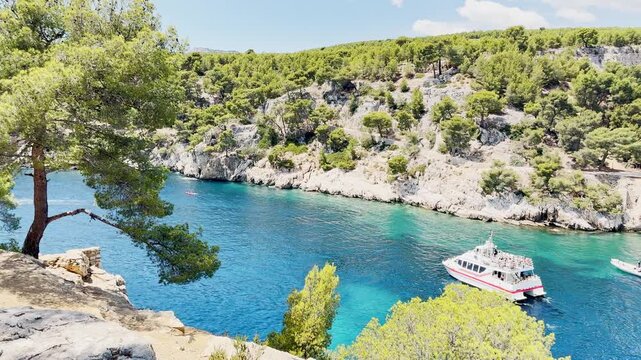 Calanque de Port Miou bay seen from the sea with lush vegetation and tourist boats entering the inlet to admire scenic views, turquoise Mediterranean water on the French Riviera, near Cassis, France.
