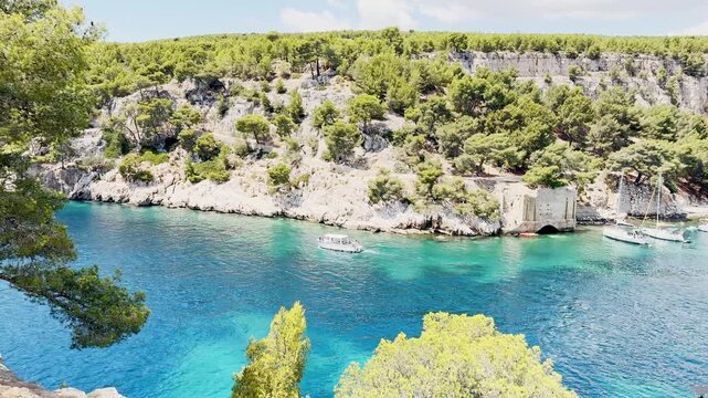 Calanque de Port Miou bay seen from the sea with lush vegetation and tourist boats entering the inlet to admire scenic views, turquoise Mediterranean water on the French Riviera, near Cassis, France.