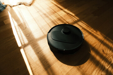 Robot Vacuum Cleaner on Wooden Floor Illuminated by Sunlight Creating Shadows in a Home Environment During Daytime