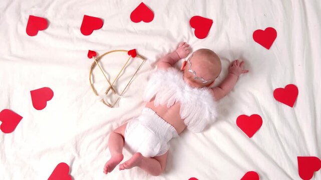 Cute smiling malshy in a Cupid costume on a white background with a bow and arrow in the shape of a heart. Happy Valentine's Day concept.