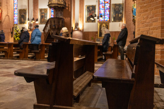 Catholic church interior with empty wooden pews in the foreground and only a few worshippers in the background. Visual symbol of declining church attendance, secularization, and reduced participation 