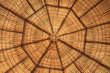 Vista inferior simétrica del interior de un techo de palapa de paja con patrón geométrico radial y textura de bambú © Mauricio
