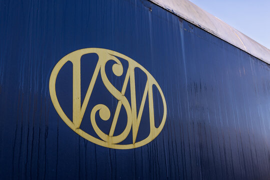 Close-up of the yellow VSM logo of the Veluwsche Stoomtrein Maatschappij on a dark blue vintage train carriage with visible rain streaks or wear. Beekbergen Netherlands, 7 November 2025.