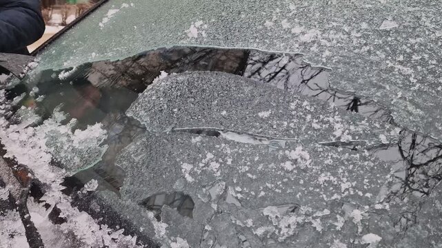 A detailed shot of a person using a plastic scraper to remove a stubborn, thick crust of frozen ice and sleet from a car window. Perfect for themes of winter maintenance, freezing weather challenges