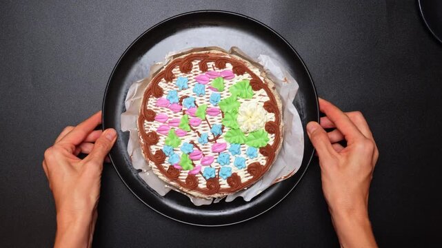 Decorating a cake with colorful icing patterns in a kitchen setting. Hands hold a decorated cake with bright icing in a kitchen. The cake has a variety of colors arranged in a pattern.