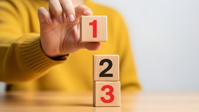A person stacking wooden blocks with numbers on a table in a simple setting with a blurred background