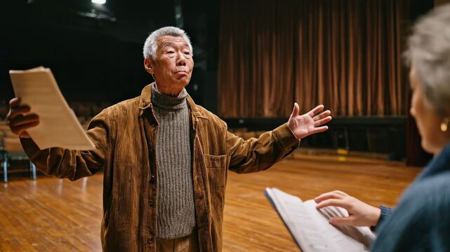 Asian senior man directing, gesturing expressively while rehearsing onstage with a younger woman. Warm tones fill the empty theater. Senior actor, emotional guidance, dramatic arts, passion.