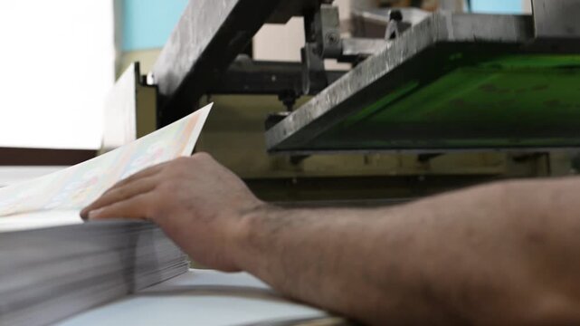 The process of silkscreen printing on a printing press in the production room of the printing house.