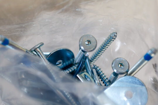 metal screws, bolts and fittings for furniture assembly in plastic bag. diy hardware set for home improvement, construction and repair projects, close up of fasteners and connectors.