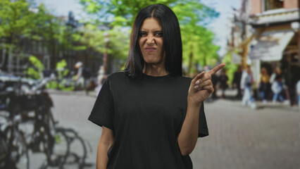 Fototapeta premium Woman pointing finger to the right with visible hand and black shirt standing in a busy urban street scene; disapproval warning.