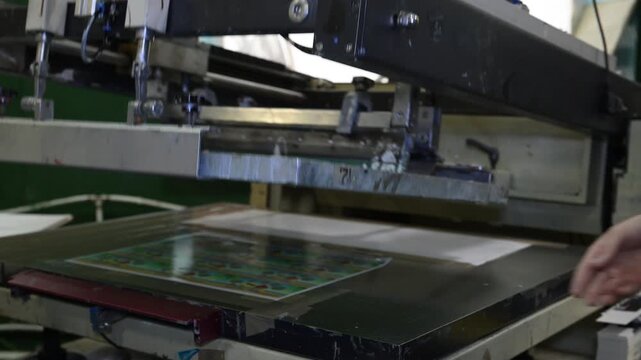 The process of silkscreen printing on a printing press in the production room of the printing house.