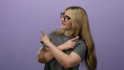 Obraz premium Woman pointing with both hands over isolated purple background, wearing glasses and a gray shirt, blonde hair suggesting a questioning attitude in modern lifestyle context.