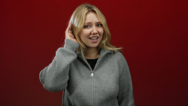 Woman expressing emotions against bold red background with blonde hair in a gray sweater.