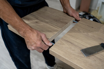 Man's hands installing a wooden panel into furniture using metal dowels, indicating diy assembly and home renovation