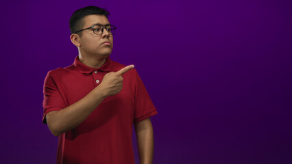 Fototapeta premium Man in red polo and glasses pointing with crossed arms and index finger in purple studio; rejection doubt.