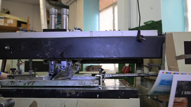 The process of silkscreen printing on a printing press in the production room of the printing house.
