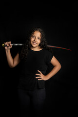 Fototapeta premium Brazilian teenager, a beautiful young Brazilian woman with a Japanese sword, low key, black background, selective focus.