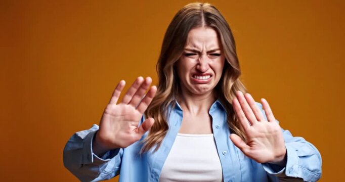 Young Woman Showing Disgust and Repulsion, Rejection Gesture in Studio Against Orange Background, 4K