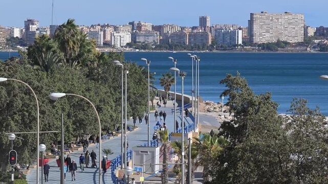 Visitors walk along the waterfront promenade near Parque de Calistenia del Postiguet in Alicante, Spain on a sunny day