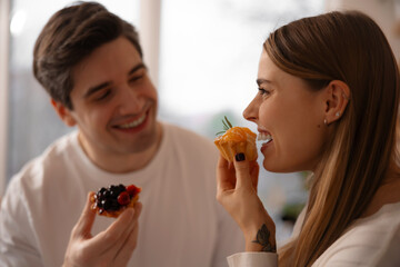 Close-up profile of a woman enjoying a mini citrus tart at home, with her partner softly blurred in the background. © My Ocean studio