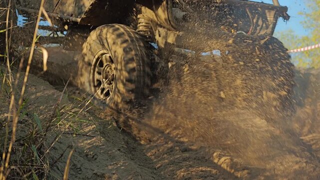 A close-up view of the wheels of an Off-road vehicle in motion during an off-road competition. Rotating tires picks up handfuls of sand, demonstrating power and speed. Slow motion