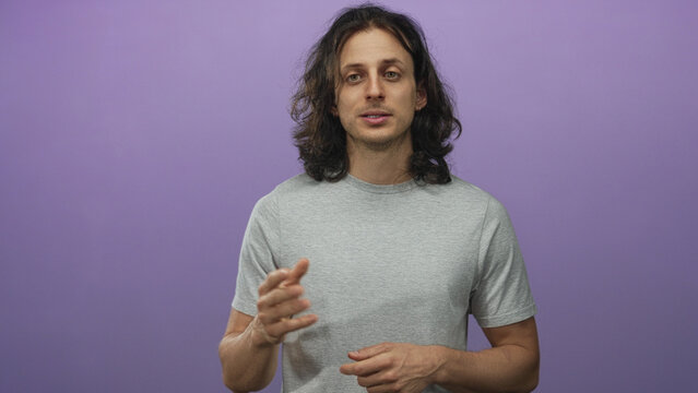 Man with long hair gesturing in purple studio, wearing grey t shirt and small earring, facing camera and speaking; calm reflection.
