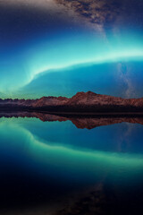 Northern Lights Over Mountain Range Reflected In Calm Alpine Lake At Night