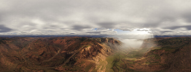 Fototapeta premium Dramatic Mountain Canyon With Fog, Sun Rays And Overcast Sky Over Rugged Valleys