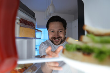 Naklejka premium Man looking into open refrigerator in kitchen, view from inside