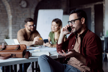 Obraz premium Businessman having a phone call in a busy open-plan office.
