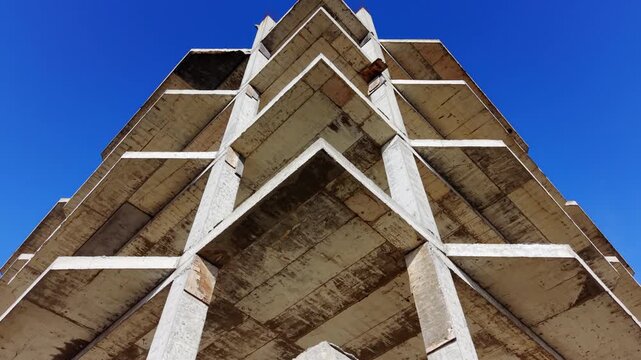 Low angle view of a sharp architectural corner of a multi-level reinforced concrete structure against a clear blue sky. Aerial view.