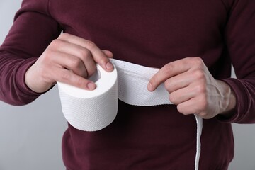 Man with roll of toilet paper on grey background, closeup
