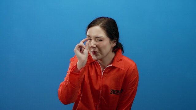 Woman in orange prison jumpsuit making small hand gesture against blue background signifies something minimal or insignificant.