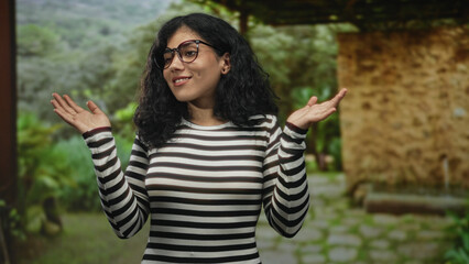 Naklejka premium Woman rubbing eyes and shrugging hands in black and white striped top near stone building on a green path; playful confusion.