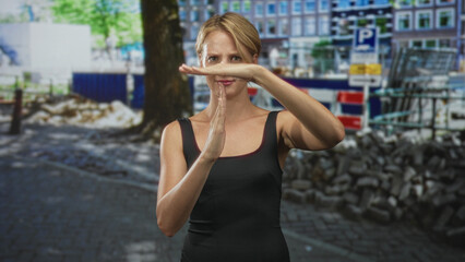 Woman shows timeout with hands in street construction area by barrier and cobblestones wearing black tanktop; confidence calm.