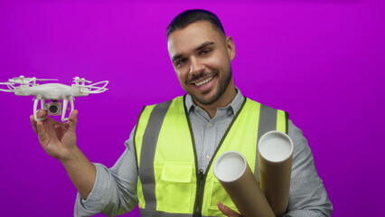 Fototapeta premium Young man holds drone in purple studio with rolled blueprint tubes; determination inspiration progress.