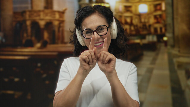 Middle age hispanic woman puckers lips for kiss and shapes a heart with fingers inside church; affection joy.