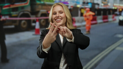 Fototapeta premium Woman smiling at construction site showing hashtag gesture wearing black outfit on urban street with people working in the background.
