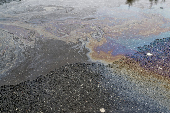 Iridescent oil and fuel streaks across puddle on asphalt.